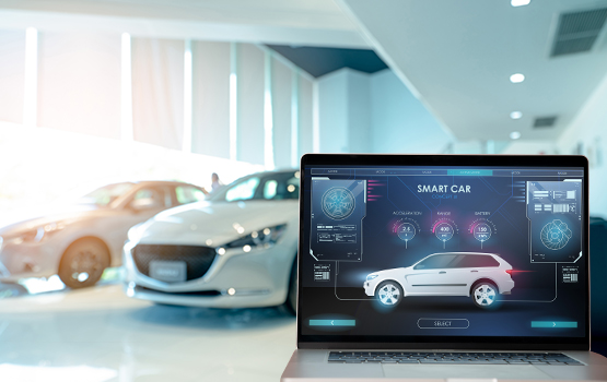 A laptop on a table in the foreground with a car visible in the background inside a dealership showroom, illustrating the integration of technology in modern auto dealerships.