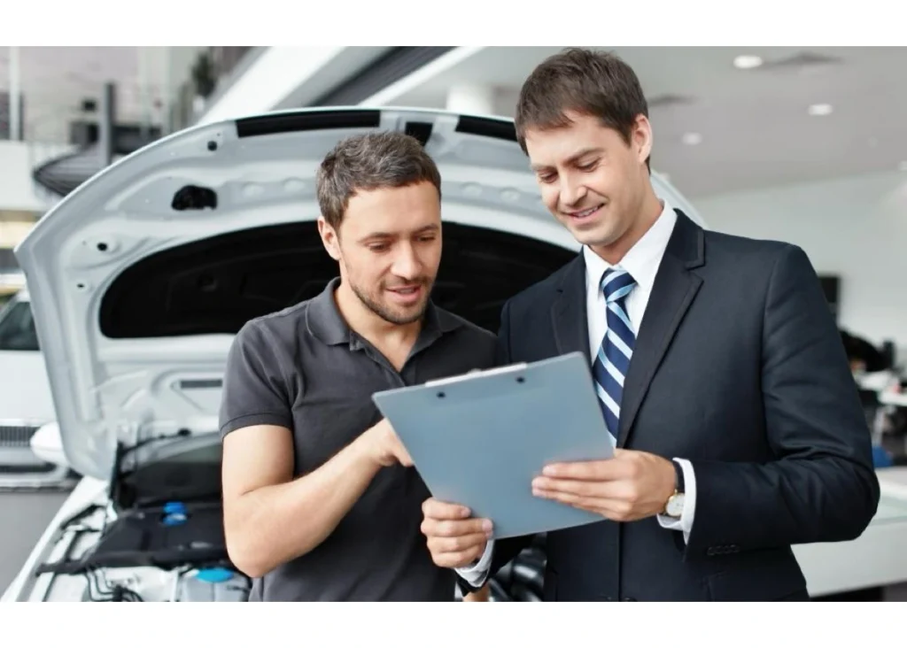 A customer and car consultant at a dealership examine car details on a sheet. With a keen eye on optimizing inventory management, the consultant helps the customer find their perfect fit.