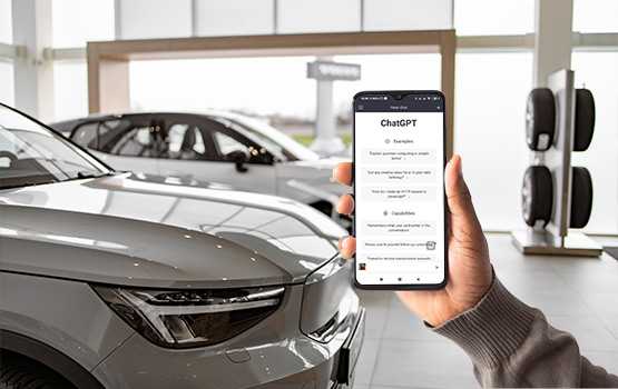 Person holding a phone with ChatGPT open in a dealership showroom, highlighting AI's role in enhancing car sales, customer service, and inventory management.