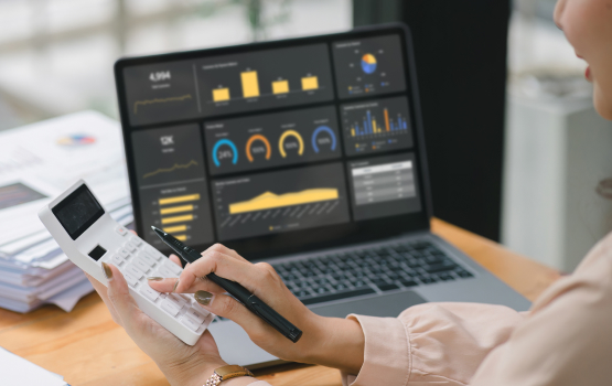 A person using a calculator while analyzing data on a laptop screen displaying charts, graphs, and business analytics.