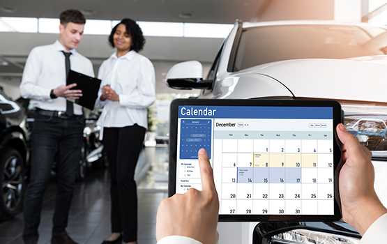 A dealership employee holding a tablet displaying a December calendar, with two colleagues discussing in the background near a white car, symbolizing year-end inventory management planning.